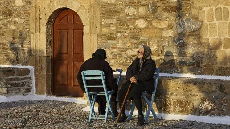 IMAGO Creative, Herbst, Reiseziel, Dodekanes, Griechische Inseln Zwei ältere Menschen sitzen auf blauen Stühlen vor einer Steinmauer und unterhalten sich, Ostern 2025, Kirche Entschlafung der allheiligen Gottesbärerin, Kimisis tis Theotokou, Asklipio, Rhodos, Dodekanes, Griechische Inseln, Griechenland, Europa Two elderly people sitting on blue chairs in front of a stone wall and talking, Easter 2025, Church of the Dormition of the All-Holy God Bear, Kimisis tis Theotokou, Asklipio, Rhodes, Dodecanese, Greek Islands, Greece, Europe Copyright: imageBROKER RalfxAdler iblraa13757715.jpg