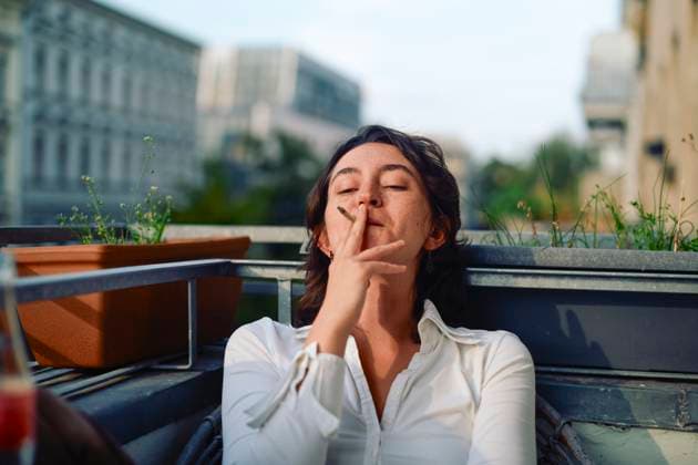 Creative Highlights Symbolbilder Woman in white shirt relaxing on a rooftop with a cigarette or joint in hand on a sunny day. bola08555 Copyright: xConnectxImagesx ,model released