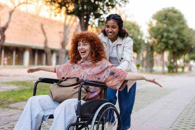 Friends enjoying a joyful moment outdoors with one providing assistance in a wheelchair model released, Symbolfoto, JCCMF13469
