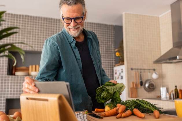 Mature man using a tablet while preparing vegetables in a modern kitchen model released, Symbolfoto property released, JCCMF13550
