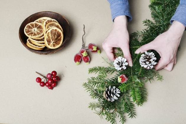Woman shows how to make classic Christmas door garland with fir twigs, cinnamon sticks, red apples and cones. Step by step, tutorial.  BEW1EB49E3E
