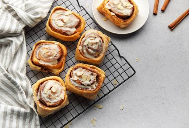 IMAGO Creative, Ostern, Bräuche, Osterbrunch Delicious cinnamon rolls with icing and flaked almonds cooling on a wire rack, perfect for a sweet treat Model Released OlenaRudo_ID28797_850633_040 Copyright: xOlenaxRudox
