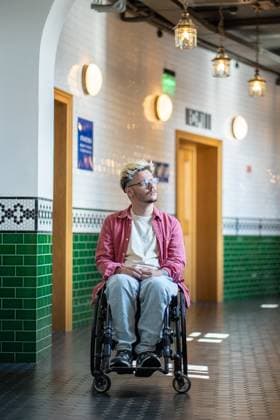 Ein nachdenklicher männlicher Student im Rollstuhl hält auf dem Flur in der Nähe eines Klassenzimmers der Universität inne und schaut zum Fenster. Thoughtful student guy in wheelchair, stop thoughtfully near lecture classrooms, reflection, gazing out of window. Accessibility in educational institutions environment for people with disabilities. (License=RF) ,model released, Symbolfoto Copyright: xZoonar.com DmitriixMarchenkox 23610028 ,model released, Symbolfoto ,property released