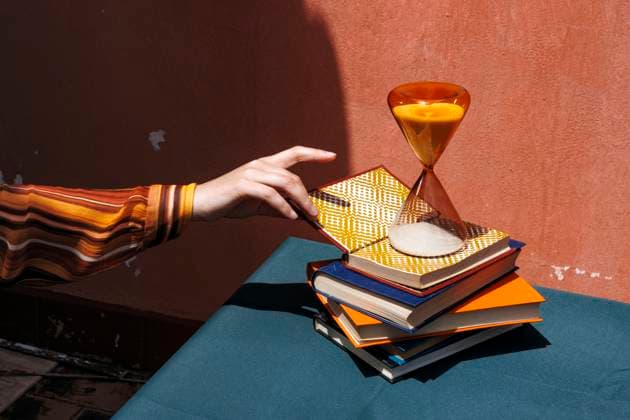 Creative Highlights Symbolbilder Hand reaching for a book on a stack with an hourglass on a table model released, Symbolfoto, RDTF00464