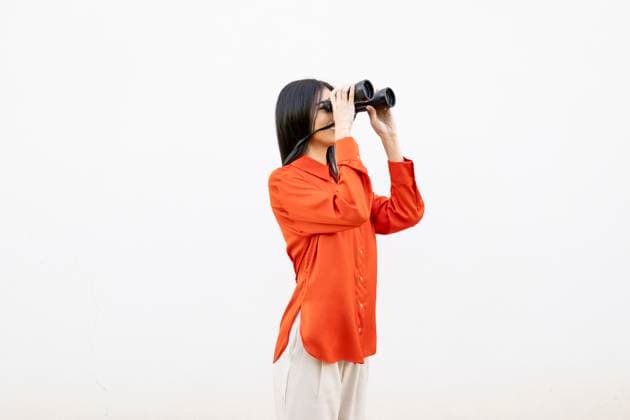 Creative Highlights Symbolbilder Woman in orange shirt using binoculars against a white wall model released, Symbolfoto, LMCF02494