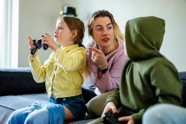 IMAGO Creative, Lifestyle, Gaming Mother talking with kids playing video games while sitting on sofa at home Sweden, Stockholm, model released, property released Copyright: xMaskotx , MA118174 MA118174