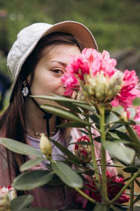 Creative Highlights Symbolbilder MR_ID29410_21441_OlhaHusonka.jpg A woman wearing a hat admires vibrant pink rhododendron flowers in a lush garden. The setting highlights a serene connection with nature and blooming beauty Model Released HannaYakimenko_ID29410_1000568_006 Copyright: xHannaxYakimenkox