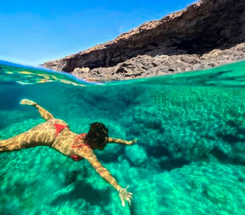 A woman wearing a red swimsuit enjoys swimming in a crystal clear natural pool surrounded by rocks in Fuerteventura, Spain. The tranquil green water highlights her peaceful swim. Model Released JuanAizpuru_ID27756_796967_010 Copyright: xJuanxAizpurux