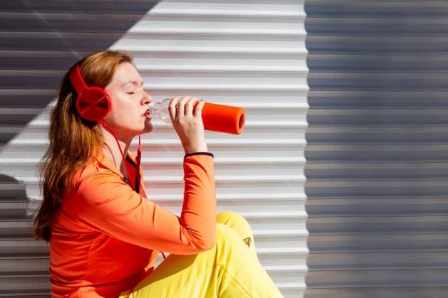Creative Highlights Symbolbilder A sporty young woman drinks water from a bottle while resting against a shutter wall after an outdoor workout. Wearing vibrant athletic clothes and red headphones, she enjoys the refreshing break Model Released Selena3726_ID29846_1008365_002 Copyright: xSelena3726x RECORD DATE NOT STATED