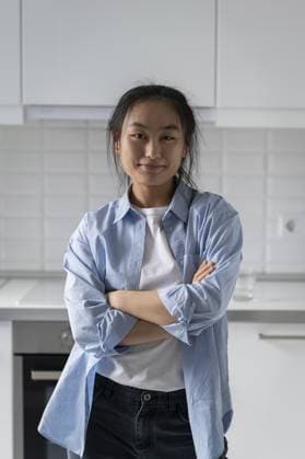 Positive glückliche asiatische Frau steht mit verschränkten Armen in der Küche der eigenen Wohnung und schaut lächelnd in die Kamera. Fröhliche optimistische chinesische Mädchen Hausfrau in lässigen ungeknöpftes Hemd und Jeans gekleidet Positive happy Asian woman stands with arms crossed in kitchen of own apartment and looks at camera smiling. Cheerful optimistic Chinese girl housewife dressed in casual unbuttoned shirt and jeans Copyright: imageBROKER DmitriixMarchenko ibxiqx14264937.jpg ,model released, Symbolfoto ,property released