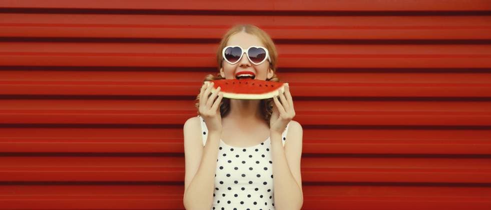 Sommerporträt einer glücklichen, lächelnden jungen Frau, die frische, saftige Früchte ißt, ein Stück Wassermelone mit einer herzförmigen Sonnenbrille auf rotem Hintergrund Summer portrait of happy smiling young woman eating fresh juicy fruits, slice of watermelon wearing heart shaped sunglasses on red background Copyright: imageBROKER VeronikaxKorneva ibxiqx14272144.jpg ,model released, Symbolfoto ,property released