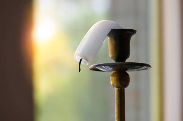 Climate symbol, a candle on a brass stand melts in the heat at the window and bends downwards Summer heat