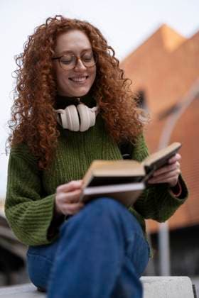 Student with red hair reading a book outdoors with headphones model released, Symbolfoto, ALZF01279