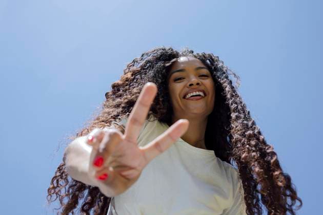 Curly haired woman smiling making peace sign outdoors model released, Symbolfoto, PGF02070