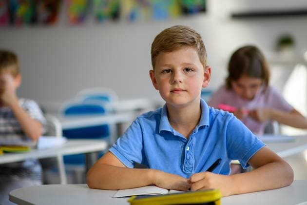 School boy sitting at the desk in classroom, looking at camera. Schoolboy sitting at the desk in classroom on the lesson, looking at camera. model released