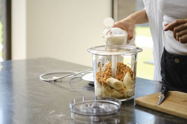 Die Zutaten werden in einen Mixer für Smoothies gegeben. Eine Person gießt Milch in den mit reifen Bananen und Sanddorn gefüllten Behälter Ingredients are being added to a blender for smoothies. A person is pouring milk into the container filled with ripe bananas and sea buckthorn Copyright: imageBROKER AlekseixIsachenko ibxfbm14562406.jpg ,model released, Symbolfoto ,property released