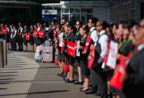 August 11, 2025, Richmond, Bc, CANADA: A passenger with luggage walks past Air Canada flight attendants as they stand during a silent protest at Vancouver International Airport on a national day of action, as labour negotiations between the Canadian Union of Public Employees and the airline continue, in Richmond, B.C., on Monday, Aug. 11, 2025. Richmond CANADA - ZUMAc35_ 20250811_zaf_c35_030 Copyright: xDarrylxDyckx