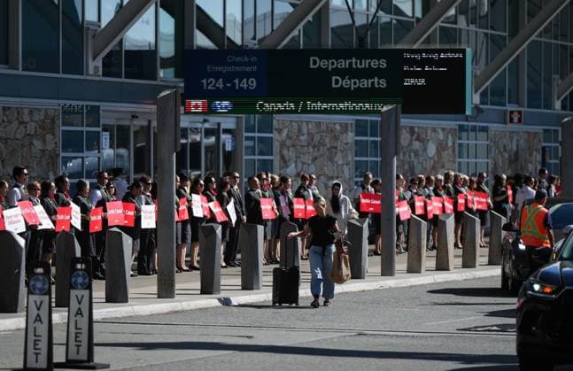 August 11, 2025, Richmond, Bc, CANADA: A passenger with luggage walks past Air Canada flight attendants as they stand during a silent protest at Vancouver International Airport on a national day of action, as labour negotiations between the Canadian Union of Public Employees and the airline continue, in Richmond, B.C., on Monday, Aug. 11, 2025. Richmond CANADA - ZUMAc35_ 20250811_zaf_c35_038 Copyright: xDarrylxDyckx