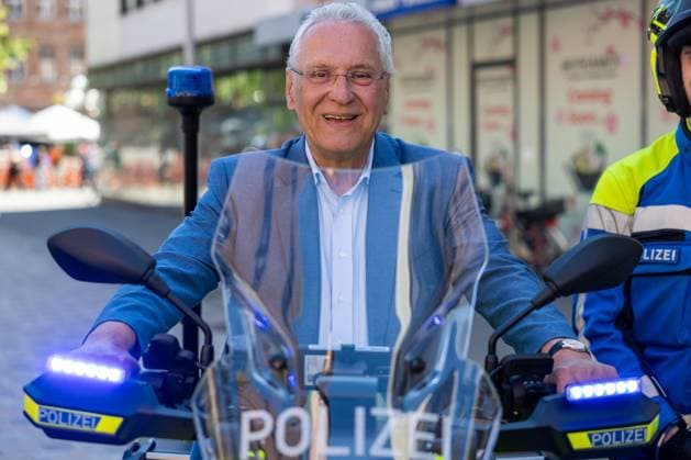 Bayerische Polizei startet Pilotprojekt mit vollelektrischen Motorrädern, Nürnberg, 12.082.2025 Portraitaufnahme von Joachim Herrmann, Bayerischer Staatsminister des Innern, für Sport und Integration, auf einem Polizeimotorrad mit eingeschaltetem Blaulicht (Symbolfoto). Herrmann trägt ein hellblaues Sakko und ein hellblaues Hemd, lächelt in die Kamera und hält beide Hände fest am Motorradlenker. Der Blick wirkt direkt und selbstbewusst. Im Vordergrund ist der transparente Windschild mit POLIZEI-Schriftzug zu sehen Nürnberg Bayern Deutschland *** Bavarian police launch pilot project with fully electric motorcycles, Nuremberg, 12 082 2025 Portrait photo of Joachim Herrmann, Bavarian State Minister of the Interior, for Sport and 20250812-6V2A6935-M4000