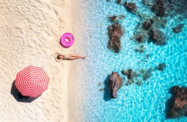 Creative Highlights Symbolbilder Aerial view of the lying beautiful woman with pink swim ring on the sandy beach, blue sea, stones, red umbrella at sunset. Summer vacation. Lefkada island, Greece. Top view of slim girl, azure water Model Released DenisBilytskyi_ID30691_1038775_024 Copyright: xx