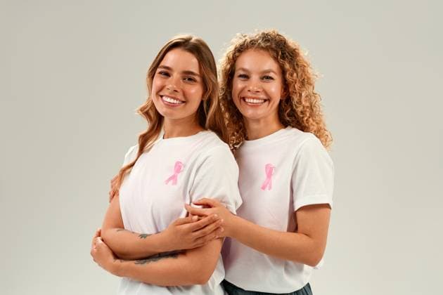 Two smiling women in white shirts with pink ribbons supporting breast cancer awareness Two cheerful women in white shirts with pink ribbons embrace and smile on white background promoting breast cancer awareness and solidarity Model Released OrionProduction_ID30910_1048090_038 Copyright: xx