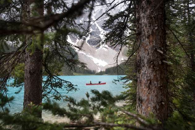 View through evergreen trees of red canoe on blue lake Moraine Banff, Alberta, Canada CR_XKTU250812A-1803084-01 EDITORIAL USE ONLY