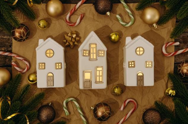 Three porcelain houses with festive decorations on the table. Three beautiful white porcelain houses in a row and a festive decoration of Christmas balls, Christmas tree branches, Christmas candy canes and gold tinsel lies around a frame on a craft paper napkin on a wooden table, flat lay very close up. Holiday preparation concept., 64100178.jpg RECORD DATE NOT STATED