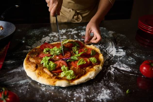 A chef slicing a homemade pizza with fresh tomato and basil toppings A close-up of hands skillfully slicing a freshly baked pizza topped with tomatoes and basil. Perfect for themes of cooking, culinary arts, and Italian cuisine., model released, , 63458242.jpg RECORD DATE NOT STATED