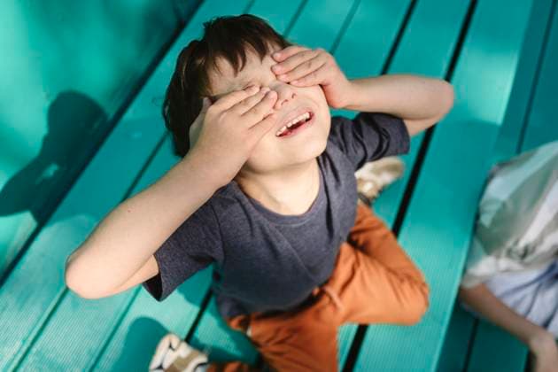 Creative Highlight Symbolbilder Boy hiding eyes with hands while playing outdoors in summer sunlight model released, Symbolfoto, EYAF03456