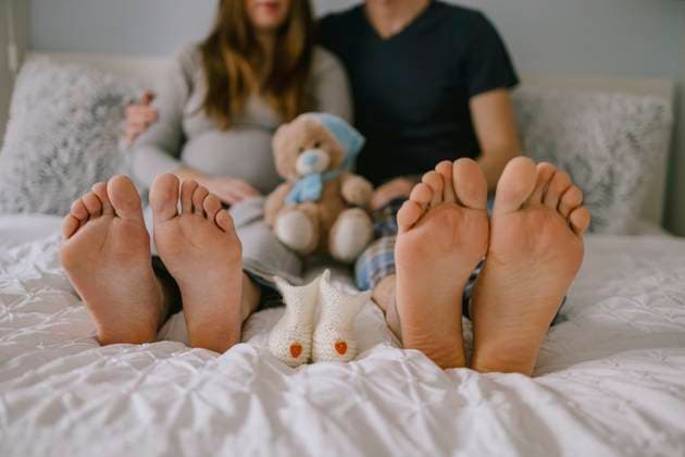 Pregnant woman and husband relaxing on bed with baby shoes and teddy bear model released, Symbolfoto property released, MCHF00579