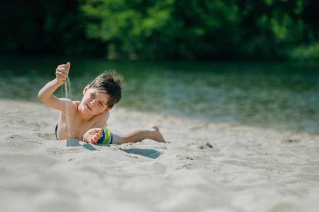 Child lying on sandy beach playing with sand on a summer day model released, Symbolfoto, ANAF04951