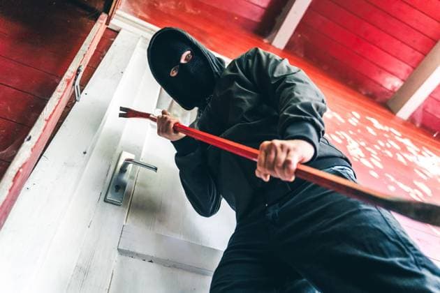 Bavaria, Germany - August 26, 2025: Masked burglar stands in front of a front door with a crowbar. Symbolic image for burglary and robbery
