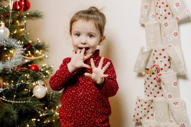 A girl licks her fingers from chocolate next to a wall advent calendar. Portrait of one beautiful Caucasian girl licking dirty fingers from gokolada while standing near a wall advent calendar and a decorated Christmas tree in the evening in the living room, close-up side view. Concept of time to receive gifts, advent calendar., model released, , 63199726.jpg RECORD DATE NOT STATED
