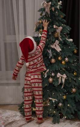 Christmas concept. a 5-year-old boy in New Year s pajamas and a Santa Claus hat stands next to the Christmas tree and joyfully decorates it. Christmas concept. a 5-year-old boy in New Year s pajamas and a Santa Claus hat stands next to the Christmas tree and joyfully decorates it., model released, , 64710198.jpg RECORD DATE NOT STATED