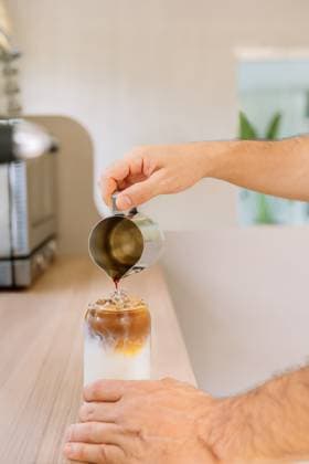 IMAGO Creative, Food, Trend, Iced Coffee PR_ID30758_11598_RandaStudio.jpg, MR_ID30758_22173_ClarenaSalamanca.jpg, MR_ID30758_22174_JorgeEnrriqueParrado.jpg, MR_ID30758_22175_LilianaAndreaLonga.jpg A person skillfully pours espresso over ice and milk in a glass, crafting a refreshing iced latte in a bright, modern kitchen. The setting is cozy and inviting, Property released Model Released AngelaRober_ID30758_1041723_022 Copyright: xAngelaxRoberx