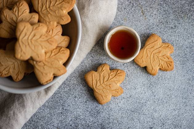 Maple leaf cookies with syrup on gray background Top view of maple leaf-shaped cookies in a white bowl on a gray background. A bowl of maple syrup accompanies the cookies, enhancing their autumnal theme. Model Released AnnaBogush_ID31032_1053000_005 Copyright: xAnnaxBogushx