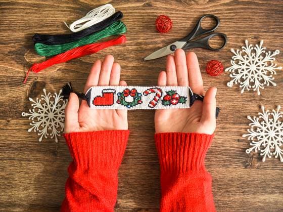 Idea for Christmas gift. Friendship bracelet with New Year alpha pattern handmade of floss threads in female hands in red sweater. Scissors, skeins of embroidery thread on wooden background. Idea for Christmas gift. Friendship bracelet with New Year alpha pattern handmade of floss threads in female hands in red sweater. Scissors, skeins of embroidery thread on wooden background., 94423348.jpg RECORD DATE NOT STATED