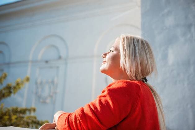IMAGO Creative, Jahreszeit Herbst in der Stadt A woman in a red sweater is sitting on a ledge. She is smiling and looking out at the street. A woman in a red sweater is sitting on a ledge. She is smiling and looking out at the street, model released, , 59746334.jpg RECORD DATE NOT STATED