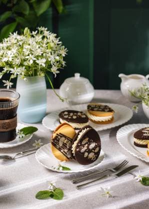 IMAGO Creative, Ostern, Bräuche, Osterbrunch Delicious easter egg shaped cookies with white chocolate filling and almonds on festive table setting Easter egg shaped cookies with white chocolate filling and sliced almonds, served with coffee on a festive table setting with spring flowers, 94709592.jpg RECORD DATE NOT STATED