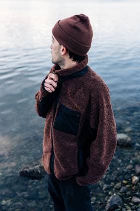 MR_ID30864_22683_NicolasMortarini.jpg A man in a cozy brown fleece jacket and beanie stands on a rocky shoreline, admiring the tranquil water. The image evokes a sense of solitude and contemplation Model Released NicoMortarini_ID30864_1046309_024 Copyright: xNicoxMortarinix