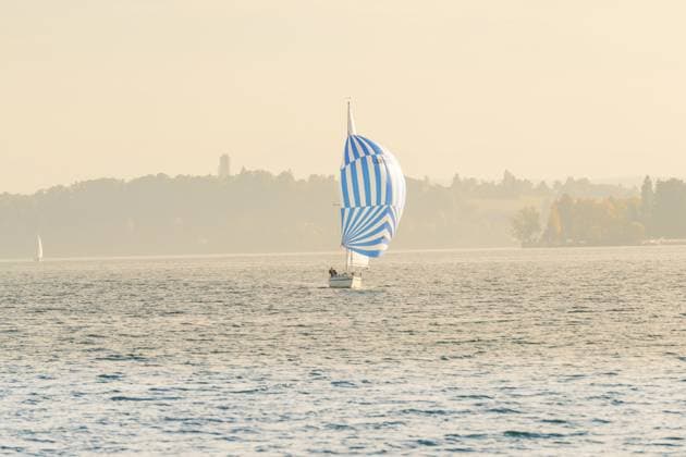 Ein Segelboot mit blau-weißem Segel auf einem ruhigen See unter einem sanften Himmel, Überlingen, Bodensee, Deutschland A sailboat with blue and white sail on a calm lake under a gentle sky, Überlingen, Lake Constance, Germany Copyright: imageBROKER ManuelxKamuf iblmlk15316369.jpg
