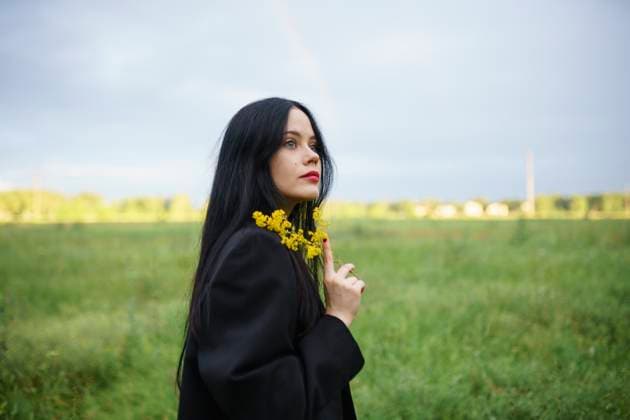 Woman in black coat holding flower in field at sunset with rainbow model released, Symbolfoto, VCF00964