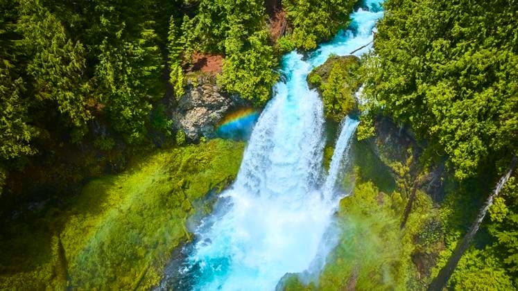 Aerial View Vibrant Sahalie Falls Cascading into McKenzie River Aerial view of Sahalie Falls on Oregon s McKenzie River, showcasing powerful cascades into a crystal blue river surrounded by lush green forests. A rainbow adds a touch of magic to this remote natural wonder., 60921222.jpg RECORD DATE NOT STATED