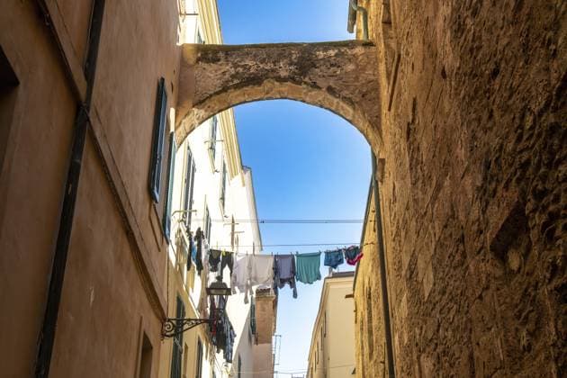 Alghero, Sardinien Italien 13.02.2025: Eine enge Gasse in Alghero, Sardinien, mit sandfarbenen Gebäuden und grünen Fensterläden. Ein Steinbogen verbindet sie, Wäsche hängt im Sonnenlicht Alghero, Sardinia - Italy - 02-13-2025: A narrow alley in Alghero, Sardinia, with sand-colored buildings and green shutters. A stone arch connects them, laundry hangs in sunlight Copyright: imageBROKER DetlefxVoigtxinfo ibliqx15431009.jpg