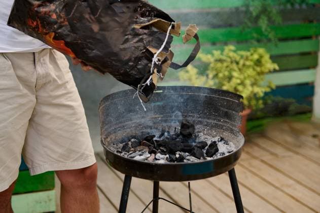 Outdoor barbecue preparation with person adding charcoal to the grill Person adding charcoal to an outdoor barbecue grill, preparing for a cookout. Relaxed and casual atmosphere in a backyard setting., model released, , property released, , 61018278.jpg RECORD DATE NOT STATED