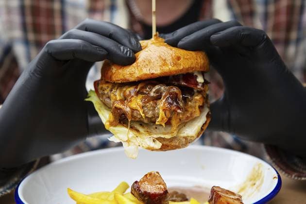 Das Konzept von Fastfood und Essen zum Mitnehmen. Ein Mann in schwarzen Latexhandschuhen hält einen saftigen Hamburger in den Händen, liegt in der Nähe von Pommes frites auf einem Metallteller zusammen mit Käsesauce The concept of fast food and takeaway food. A man in black latex gloves holds a juicy hamburger in his hands, lies near french fries on a metal plate along with cheese sauce Copyright: imageBROKER SergiyxArtsaba ibxiqx14688378.jpg