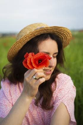 Eine junge Frau mit Strohhut hält eine leuchtend rote Mohnblume in der Nähe ihres Gesichts auf einem sonnigen Feld A young woman in a straw hat holds a vibrant red poppy flower near her face in a sunny field Copyright: imageBROKER SergiyxArtsaba ibxiqx14689869.jpg ,model released, Symbolfoto ,property released