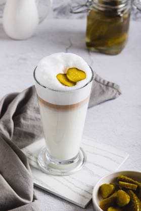 IMAGO Creative, Food, Trend, Iced Coffee Picklatte mit Schaum in einem Glas und Essiggurken in einer Schale auf dem Tisch Vertikalansicht Picklatte mit Schaum in einem Glas und Essiggurken in einer Schale auf dem Tisch Vertikalansicht (License=RF) Copyright: xZoonar.com ElenaxRuix 24106844
