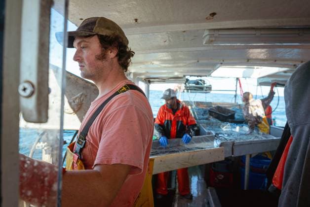 Commercial fishing and bycatch off the coast of Maine, USA - 28 Sept 2022 September 28, 2022, Portland, Maine, United States: A fisherman looking out to sea while on board a commercial fishing boat off the coast of Maine; behind him, his fellow crew members also take a break from untangling nets. A board a gillnet fishing boat, crew haul their catch of monkfish, pollock, and cod from the early hours of the morning until late at night. The fishing industry in Maine has recently taken a blow with a new set of restrictions on fishing and the environmental organization Seafood Watch recommending for people to avoid eating American lobster. This listing and regulation pose fresh threats to fishers livelihoods. While fisherfolk argue that lines Copyright: xMaileexOsten-Tanx