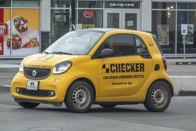 Vancouver, Britisch Kolumbien, Kanada. 10. März 2025. Ein Smart Auto, das vor einem Restaurant geparkt ist und Werbung für den gelben Checker Taxi, Limousinen und Limousinen Shuttle Service macht Vancouver, British Columbia, Canada. Mar 10, 2025. A Smart car parked outside a restaurant, advertising yellow Checker taxi cab, sedan, and limousine shuttle services Copyright: imageBROKER MarvinxSamuelxTolent ibliqx15460865.jpg